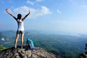 strong confident woman hiker open arms at on mountain peak rock
